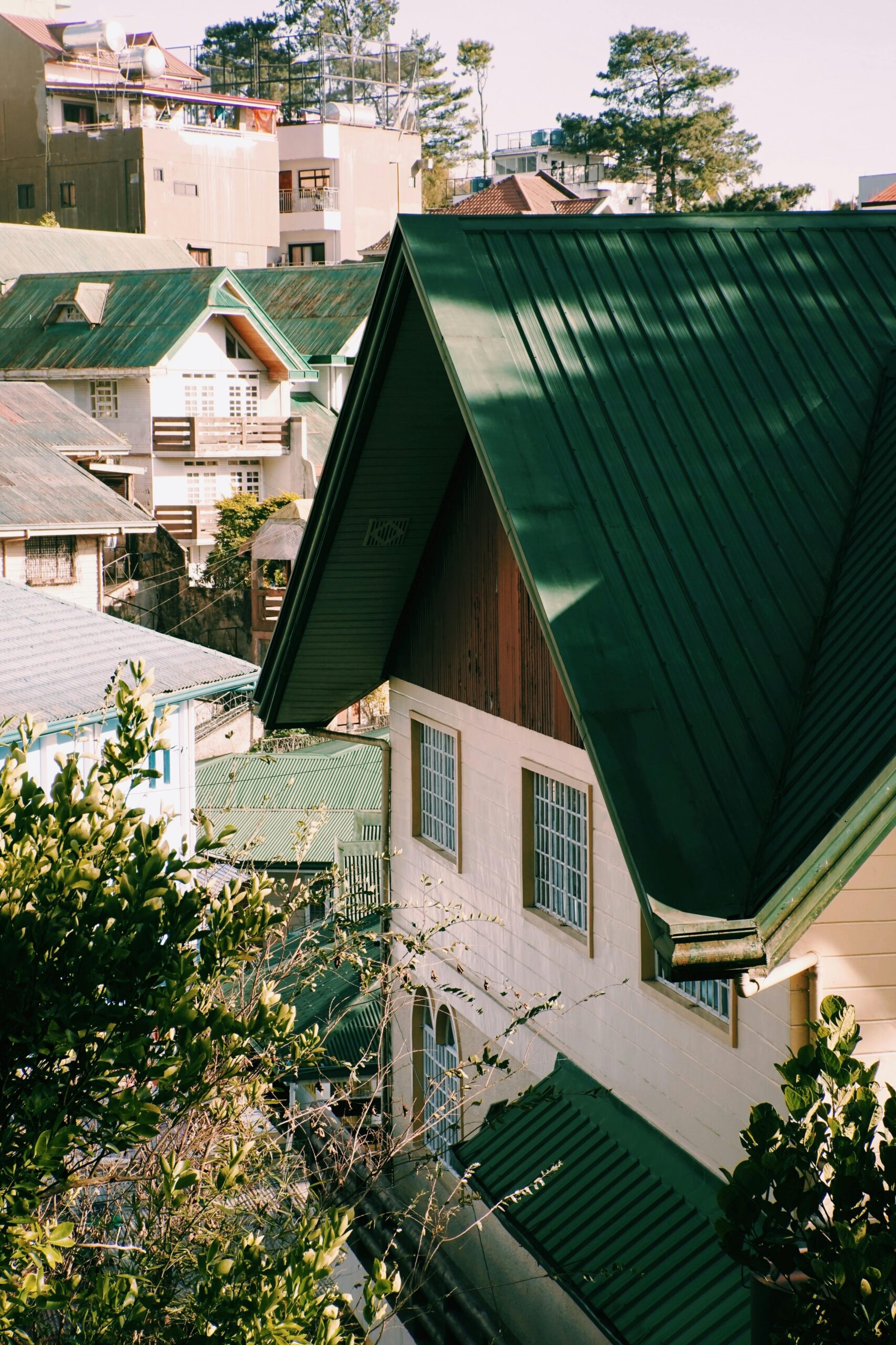 A picturesque view of townhouses featuring green metal roofs surrounded by sunlight and lush trees.